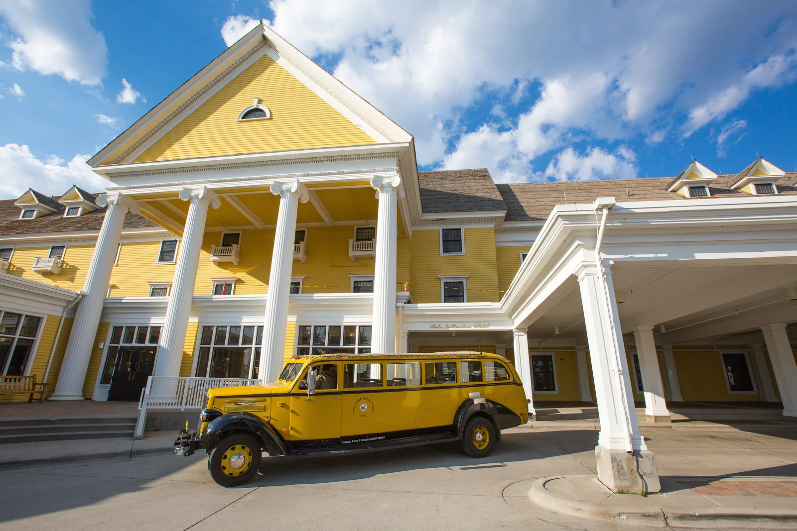 A historic yellow touring bus parked outside the white-columned Lake Yellowstone Hotel